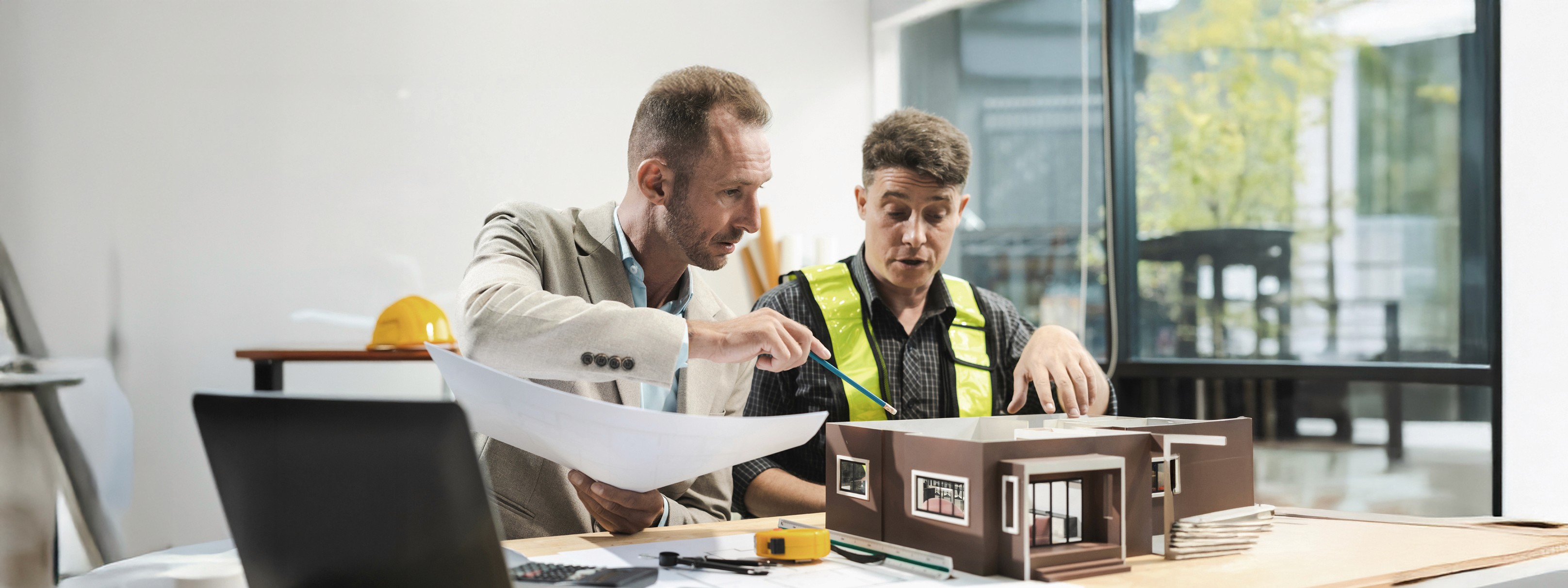 Architect en bouwheer die een maquette van een eengezinswoning bespreken.