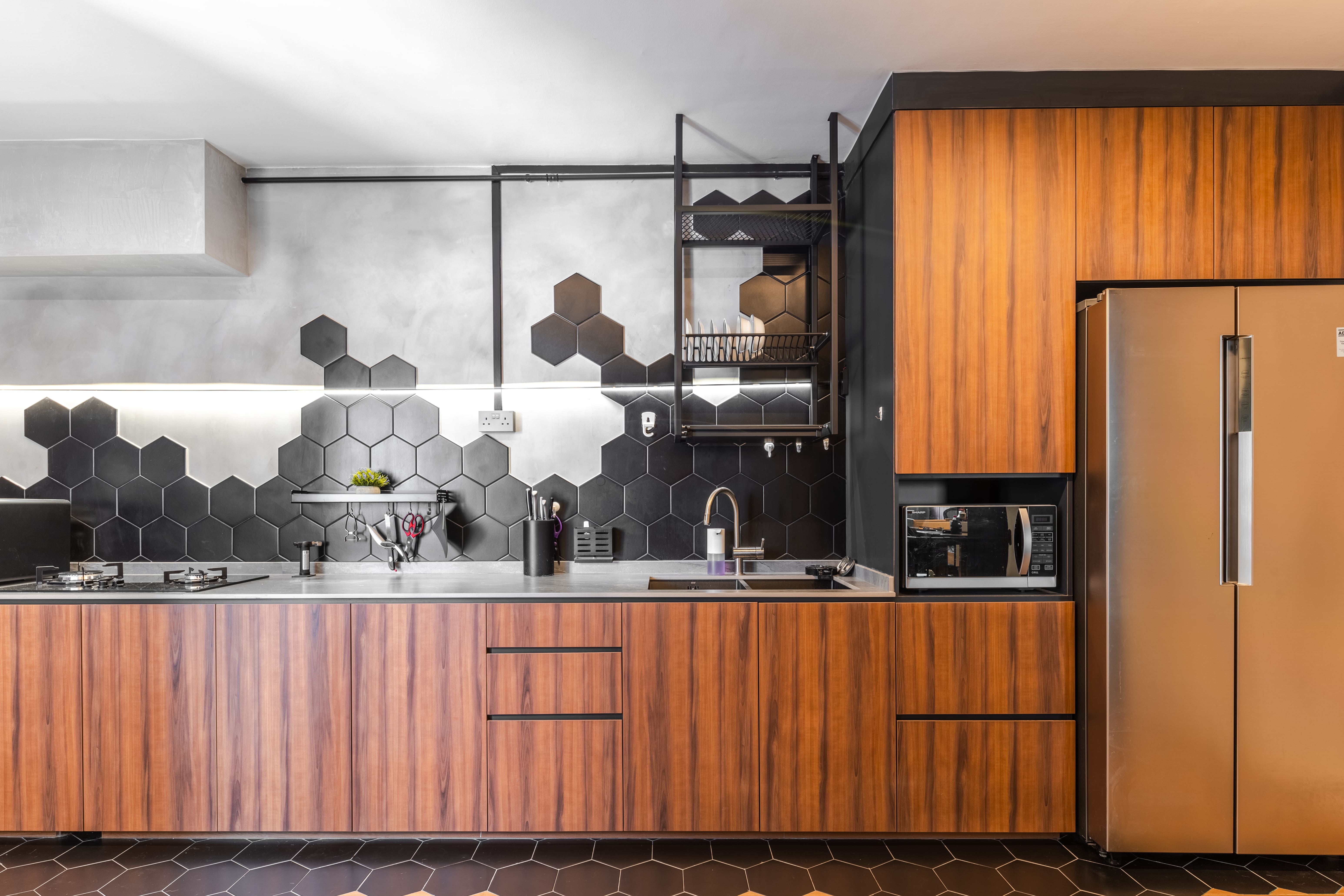 Full kitchen view highlighting wood cabinetry, integrated appliances, and striking black hexagonal backsplash design.