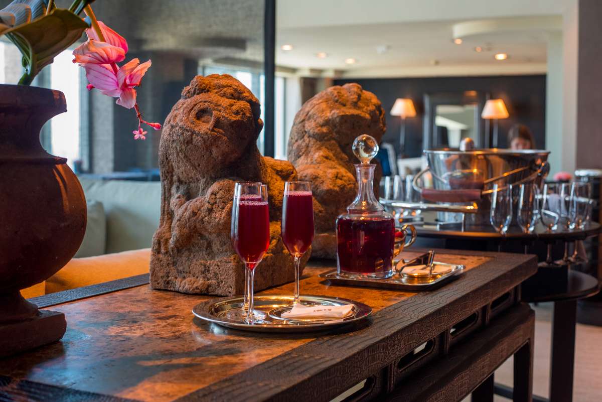 Two wine glasses and a decanter sit on a wooden bar counter in front of two stone-carved bear sculptures.