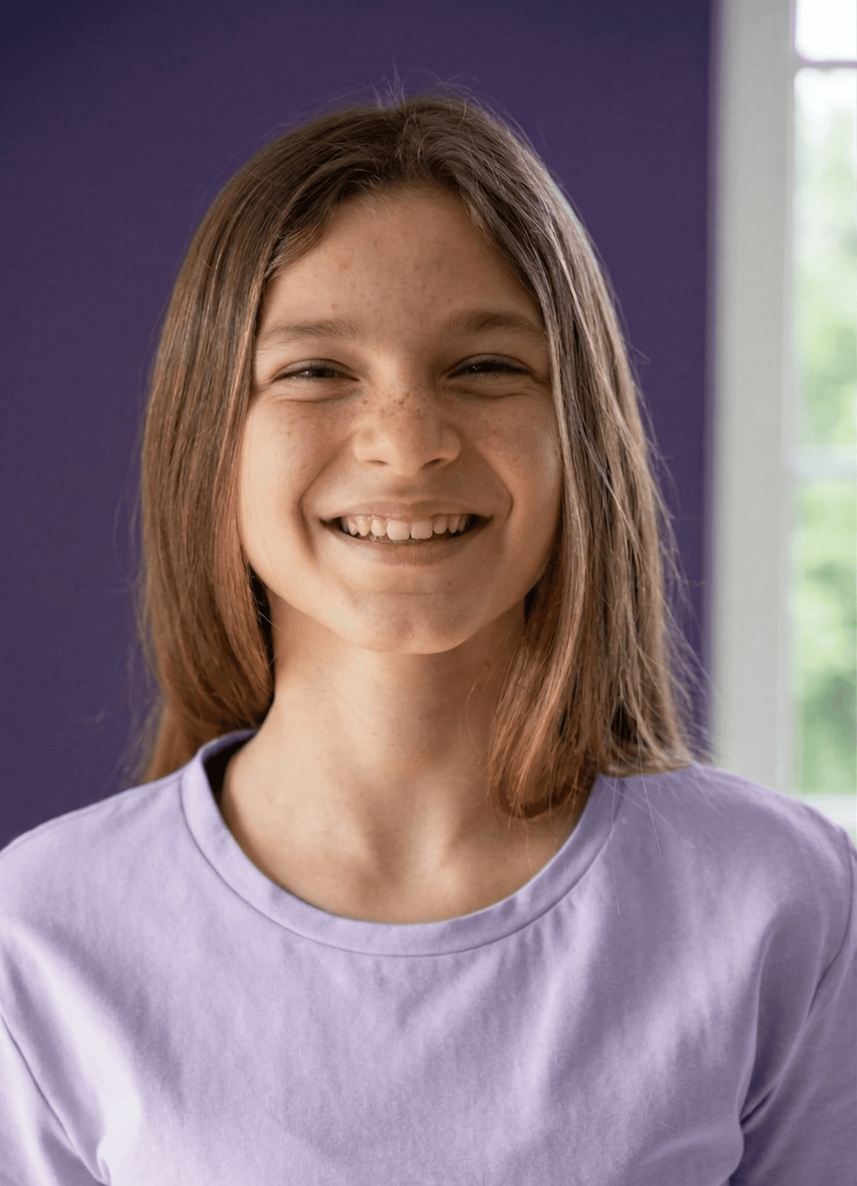 A smiling child in orange fisherman sweater and light purple parka