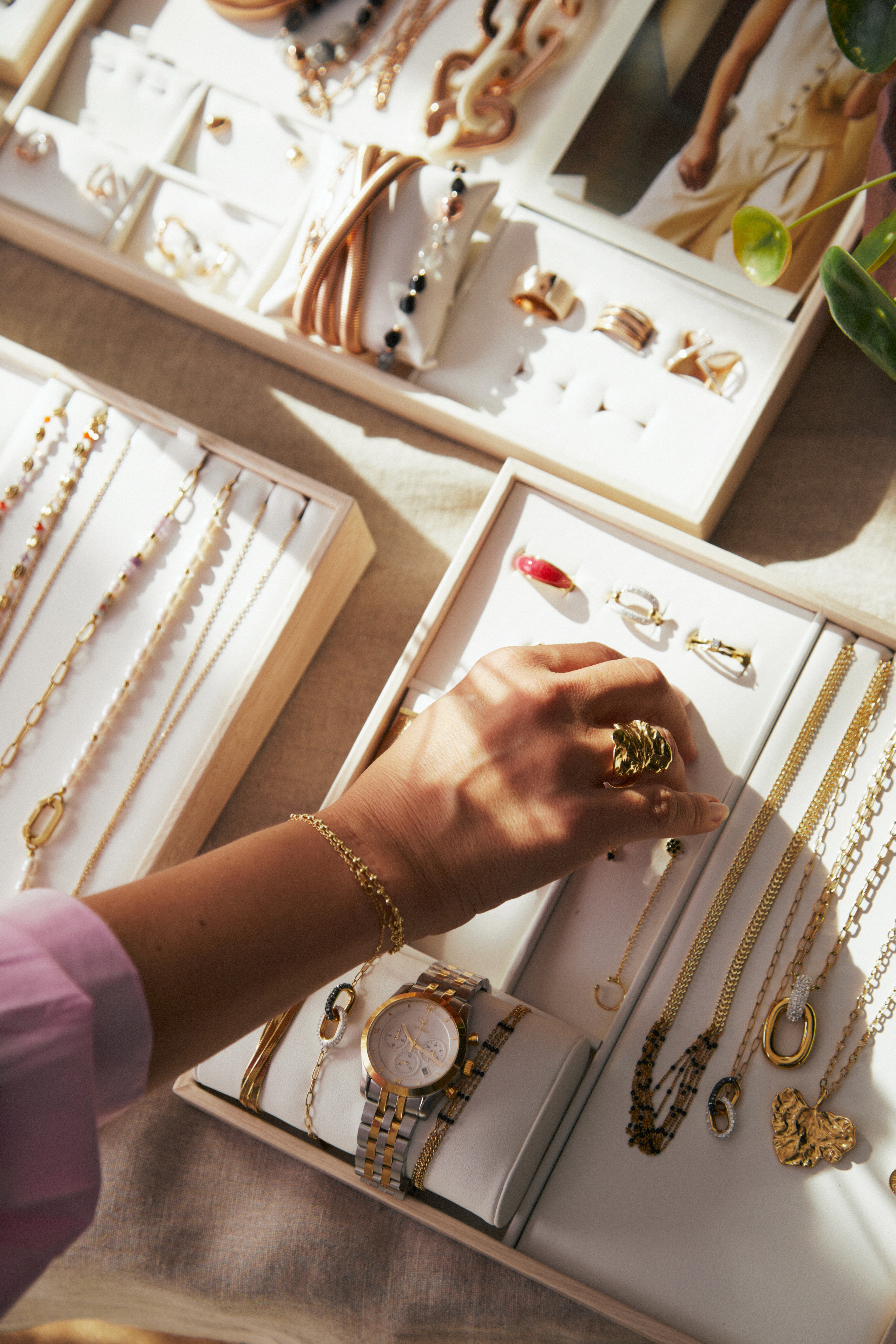 Eine Person greift zu einem Tableau mit Schmuck; warmes Licht fällt auf die Seiten und den Arm.