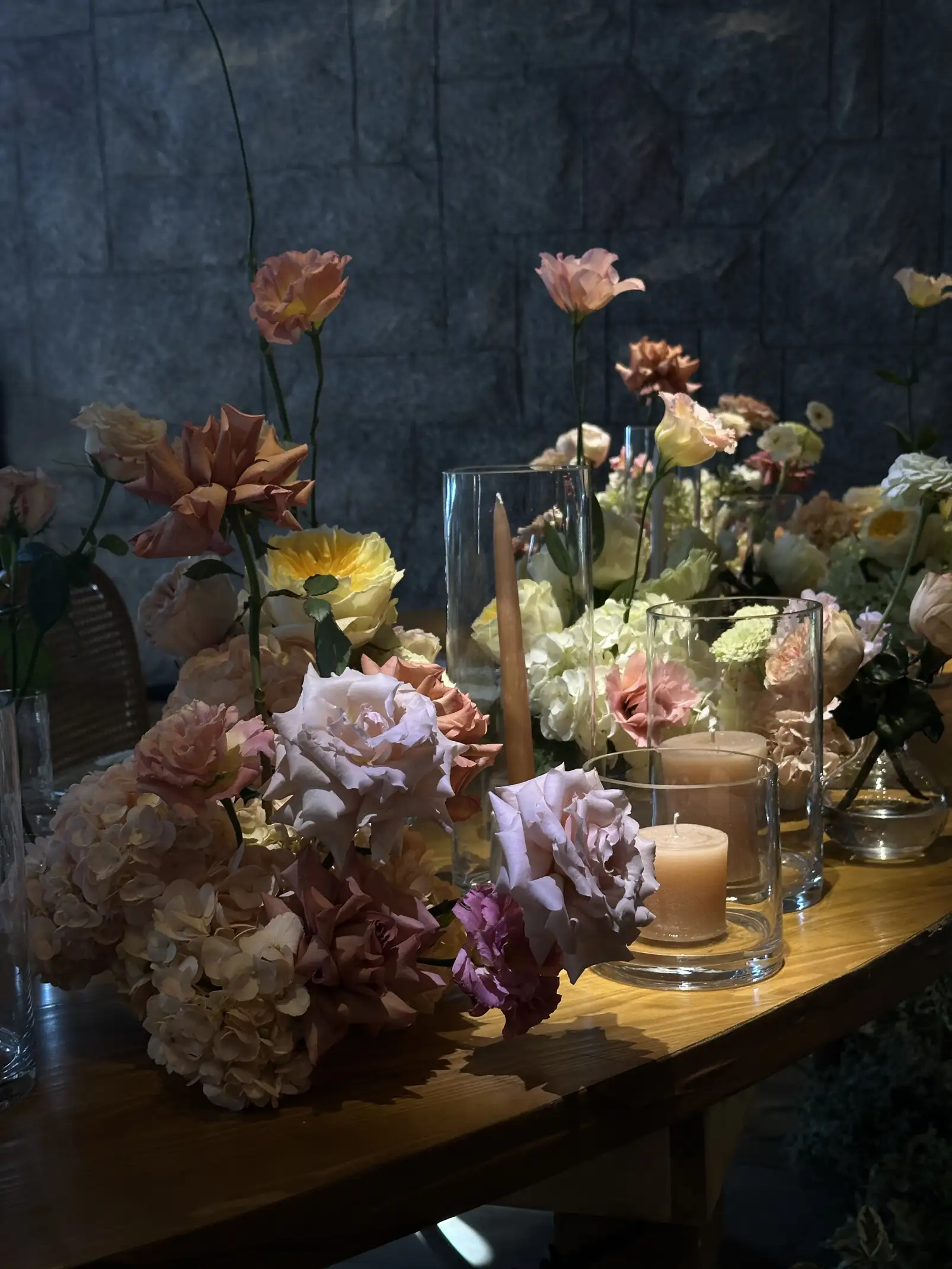 Detalle de centro de mesa con flores en tonos pastel, velas y texturas naturales sobre madera.