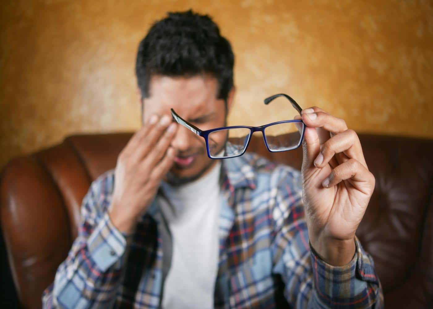 Man rubbing his eyes from eye strain while holding his glasses away from him