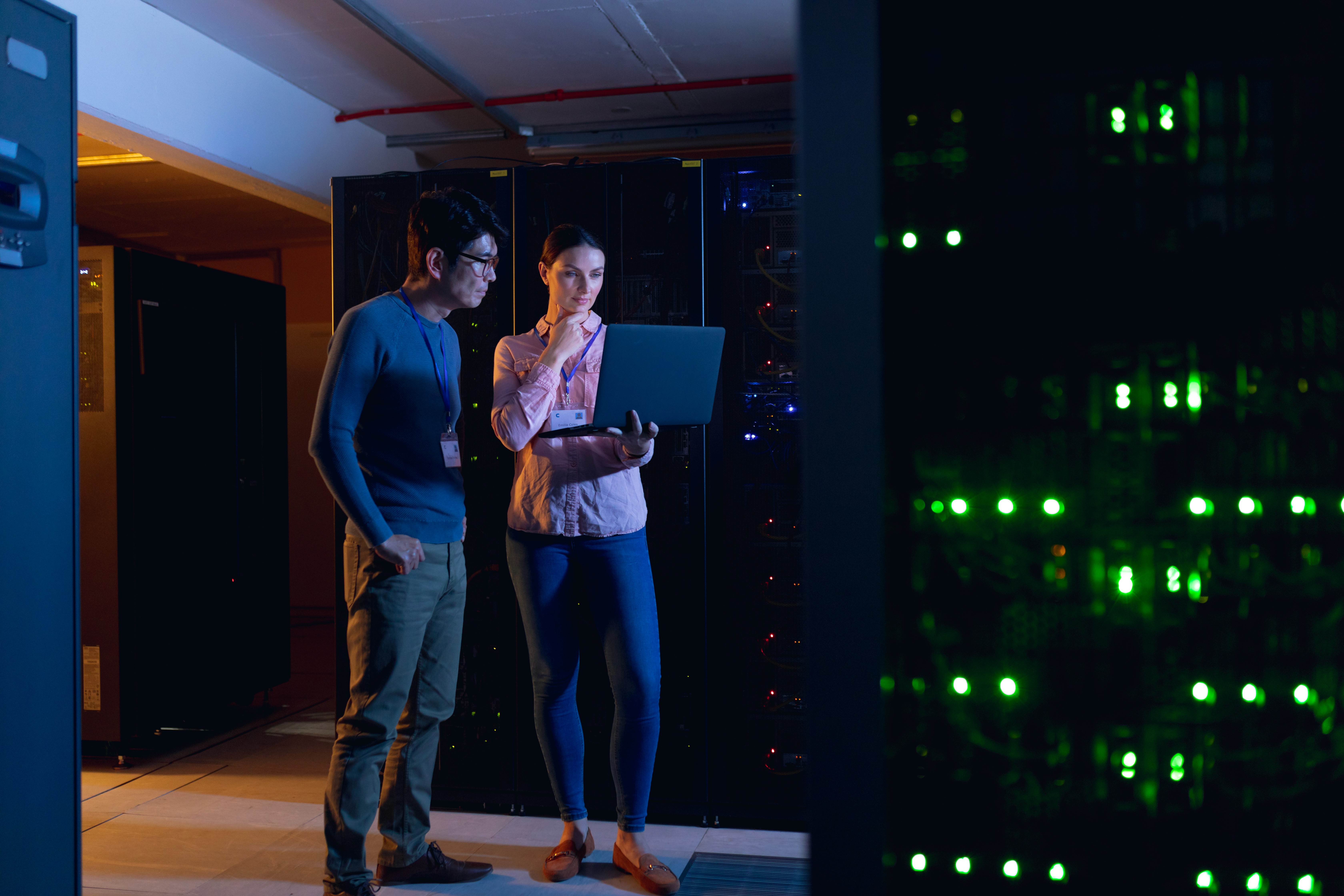 Smiling man in a maroon sweater working at a computer in a modern, industrial-looking lab or tech workspace.