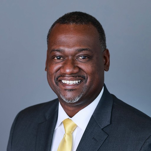 A young woman with long brown hair smiles warmly against a green background, dressed in a black jacket and white shirt.