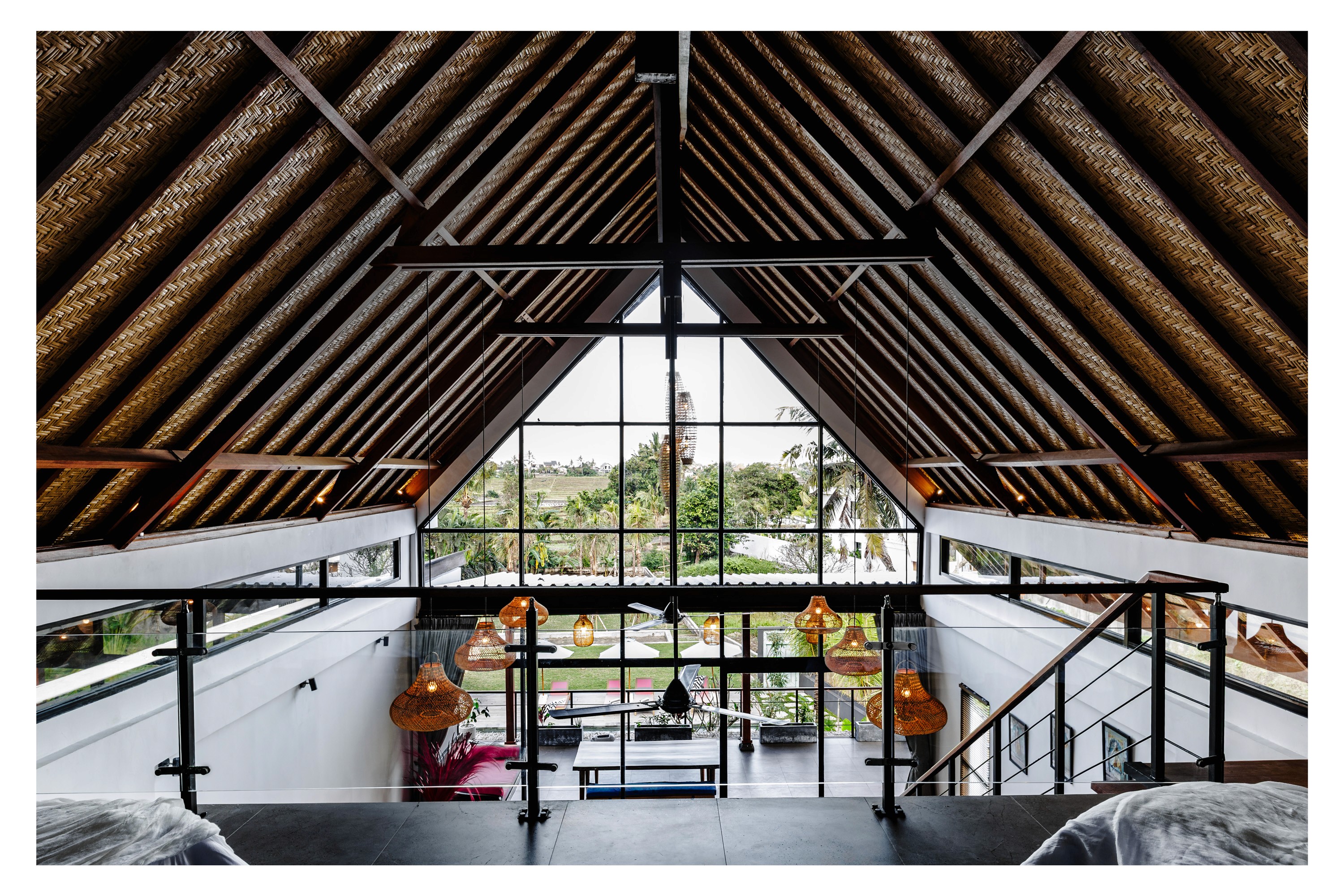 Loft interior with high vaulted ceiling, woven rattan roof, and large glass window overlooking garden.