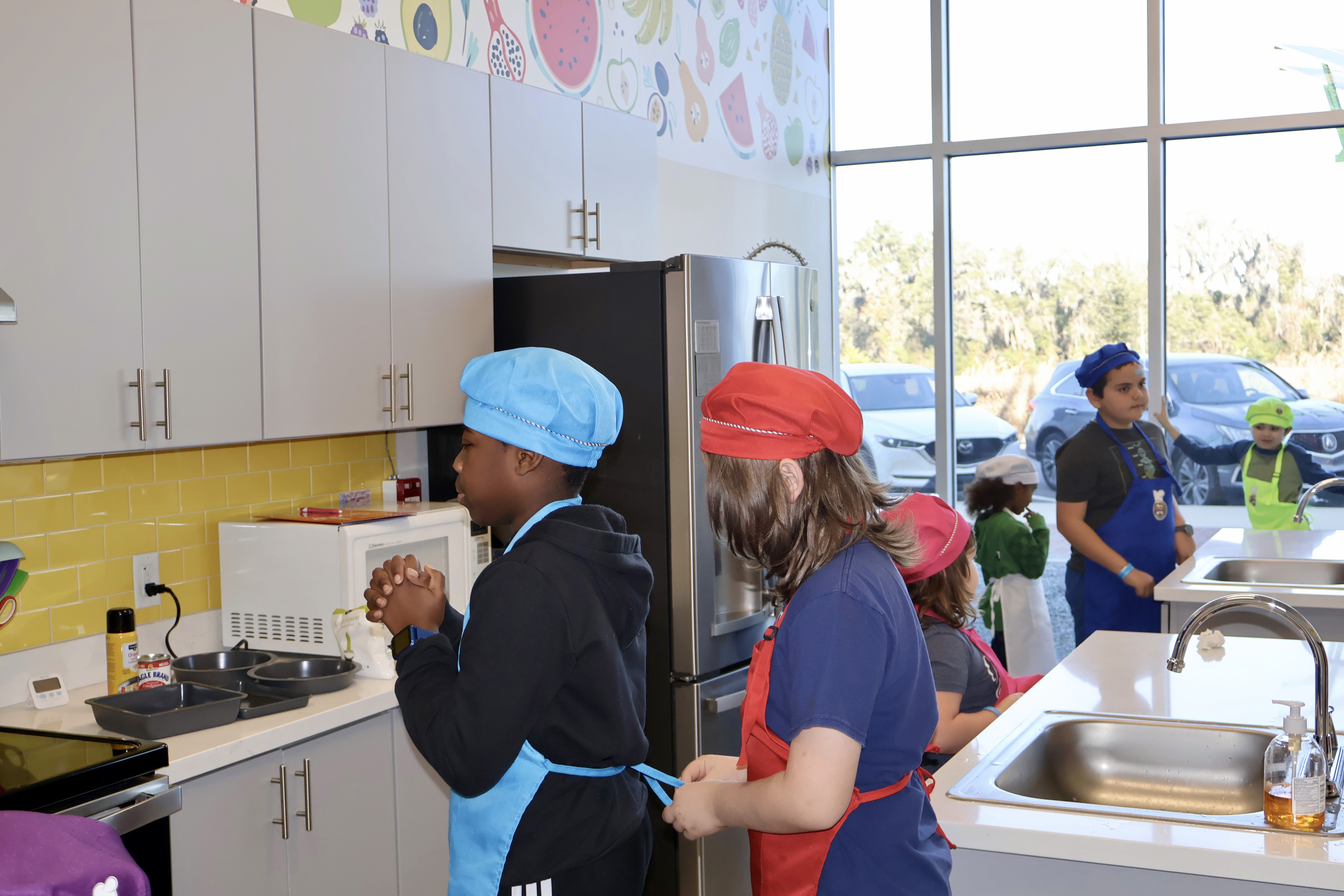 Children in colorful chef hats and aprons prepare for a cooking class
