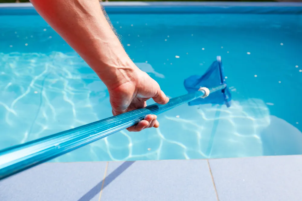 Close-up of a person using a pool vacuum to clean clear blue water.