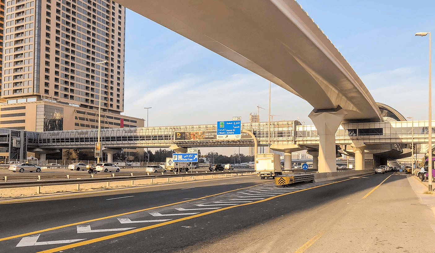 A busy highway in Al Sufouh 2, featuring cars and trucks driving beneath a large overpass.