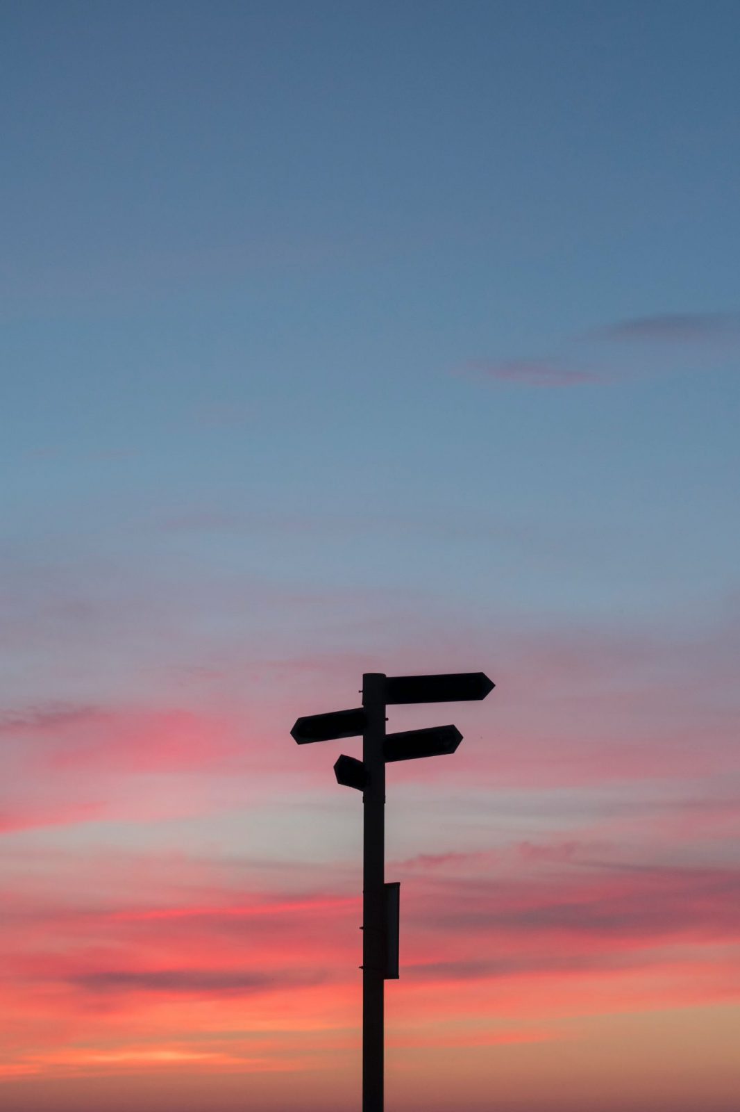 A silhouette of a signpost against a colorful sunset sky with pink and blue hues.