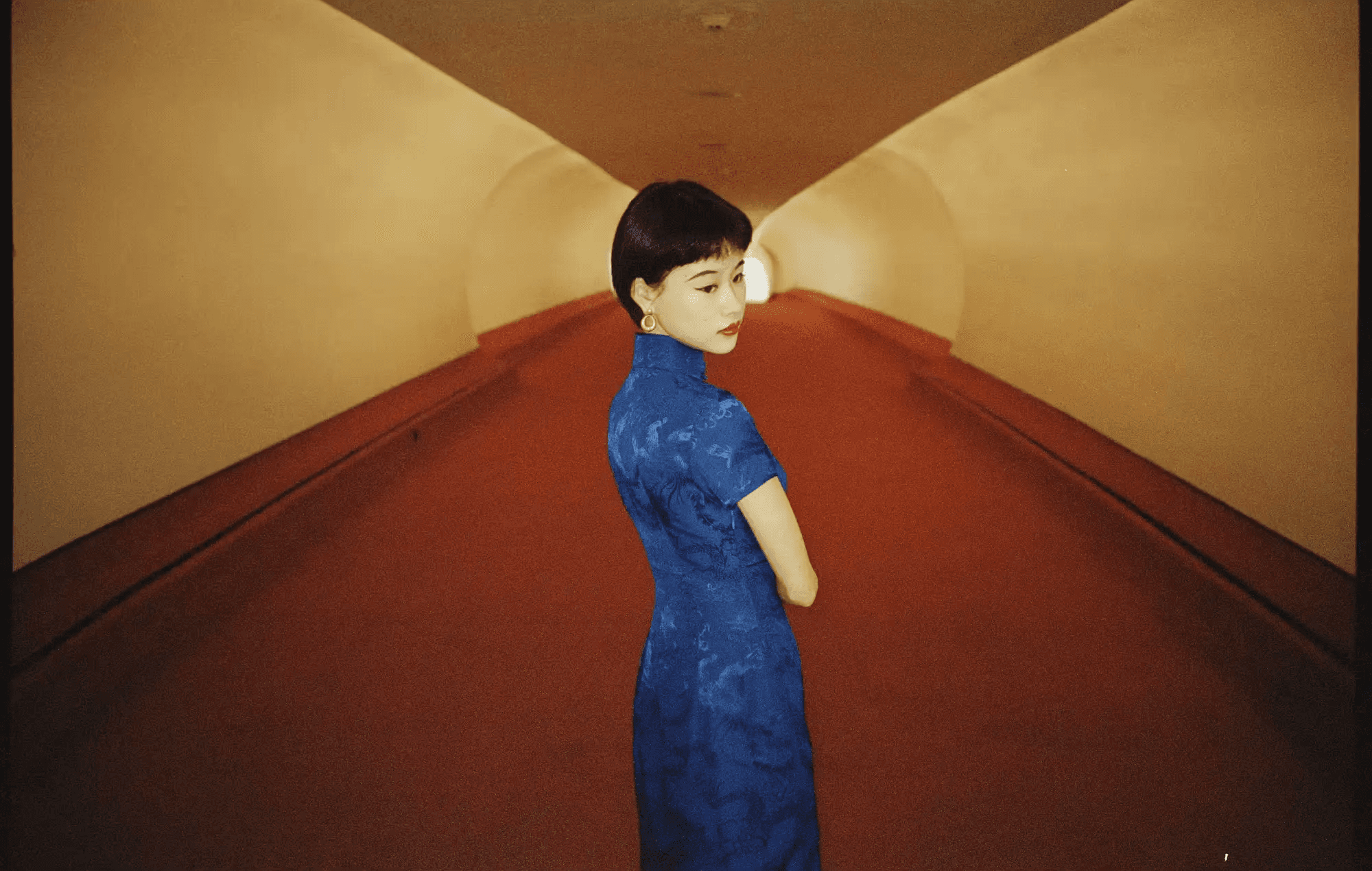 女人穿蓝色旗袍站在红色走廊中
