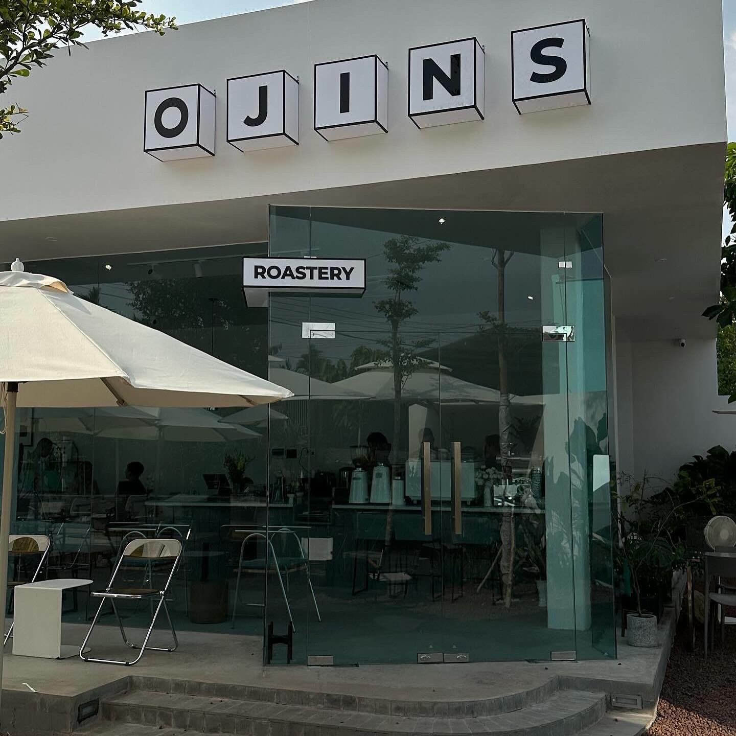 Exterior view of a store named "GJINS," featuring large windows and outdoor seating.