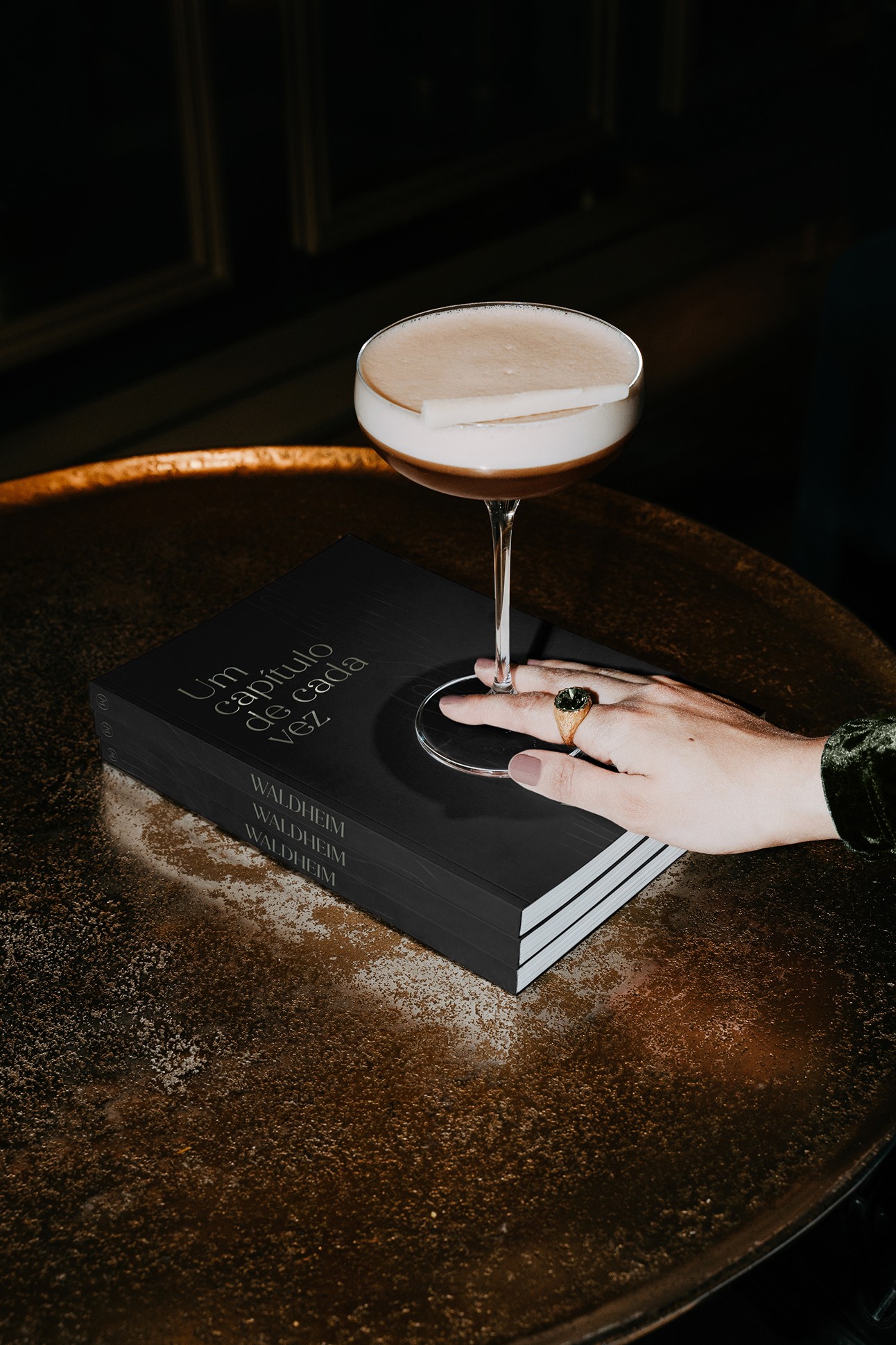  Livro institucional com copo de cocktail e mão repousada sobre a capa.