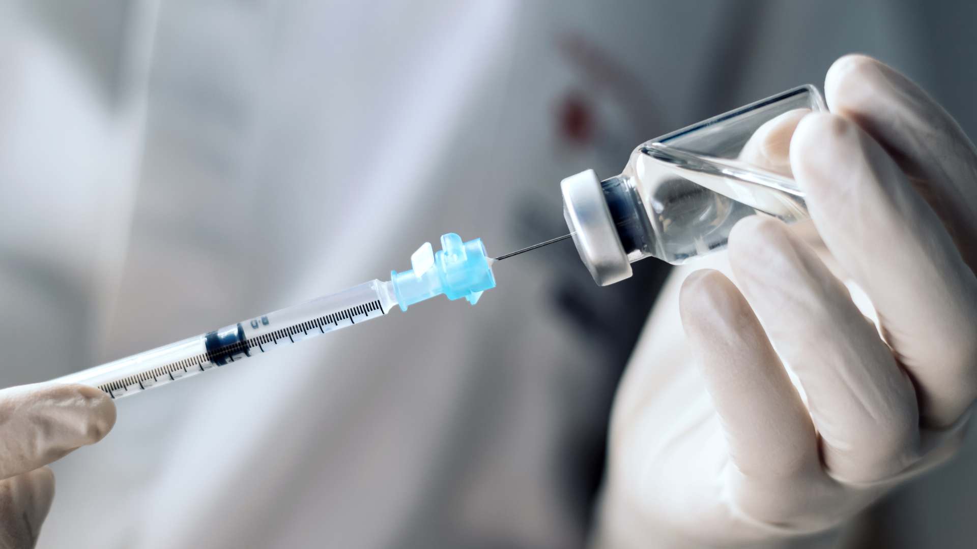 Gloved hand drawing liquid from a medicine vial into a syringe