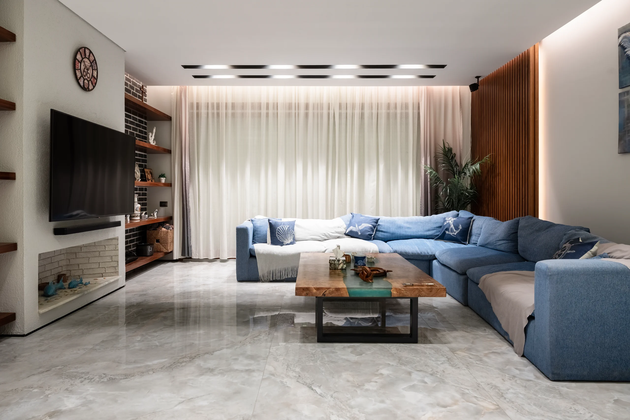 Open-plan living room at Caesar SODIC Villa with blue seating, large-format porcelain flooring and warm walnut details.