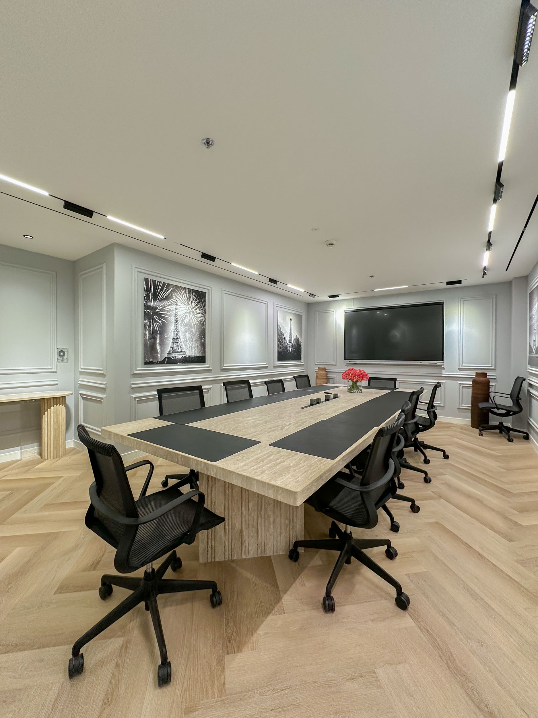 Modern conference room with a long table, black chairs, pendant lighting, and city view