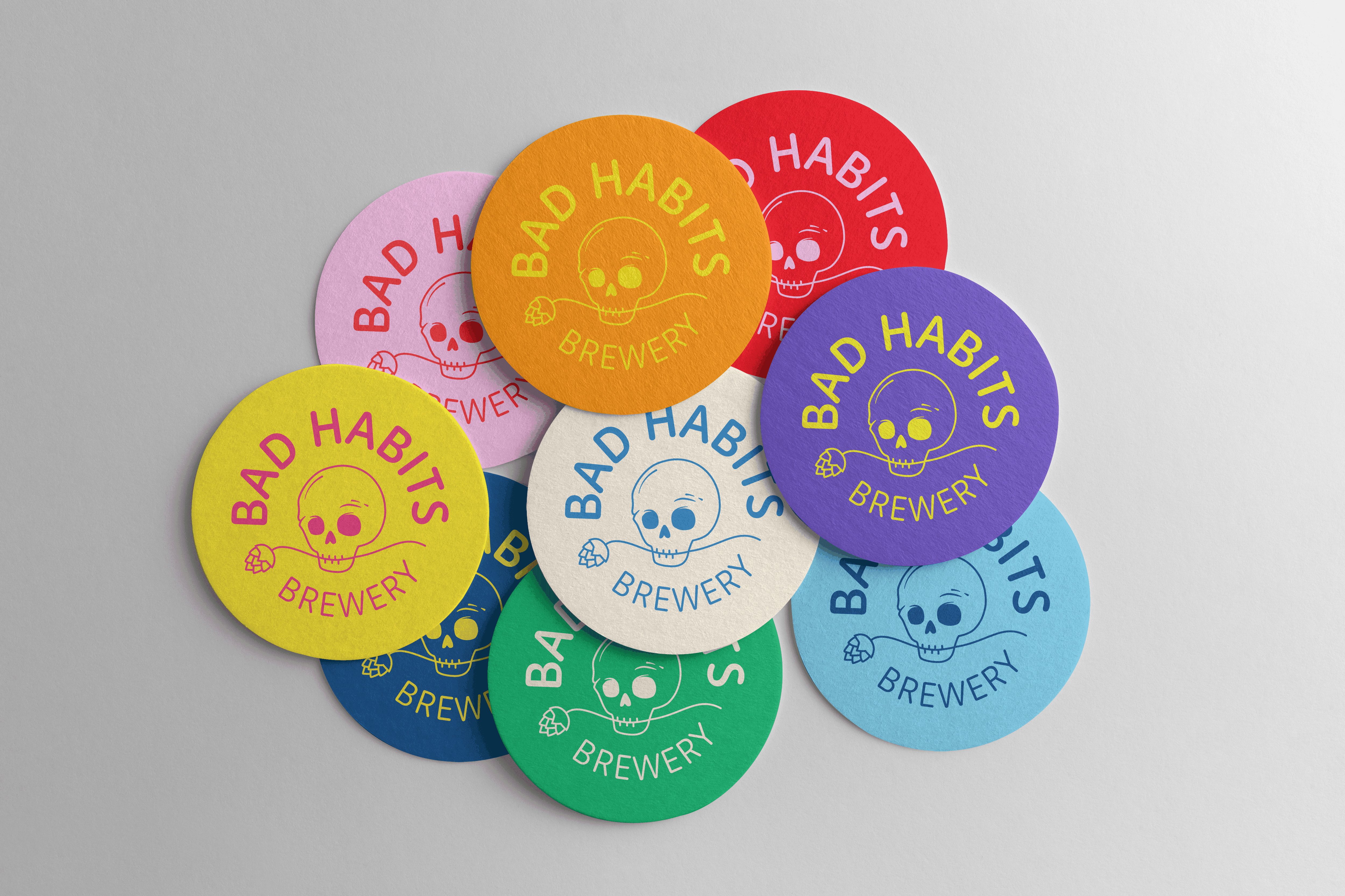 A scattered pile of colorful Bad Habits Brewery round paper beer coasters featuring a skull and hops logo.