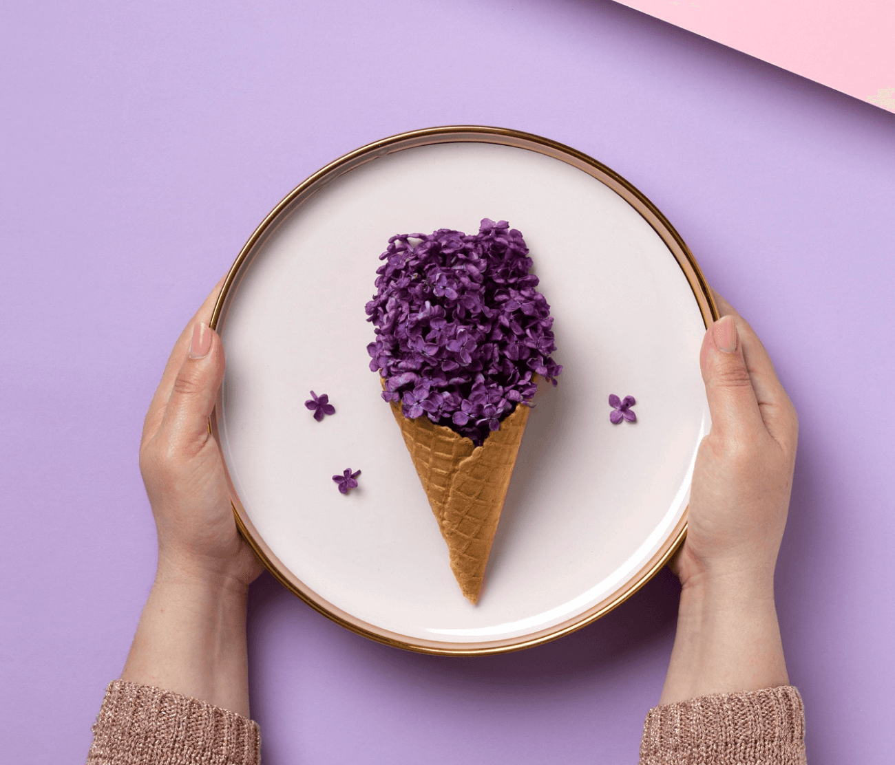 Overhead view of hands holding a plate featuring a waffle cone topped with purple lilac flowers