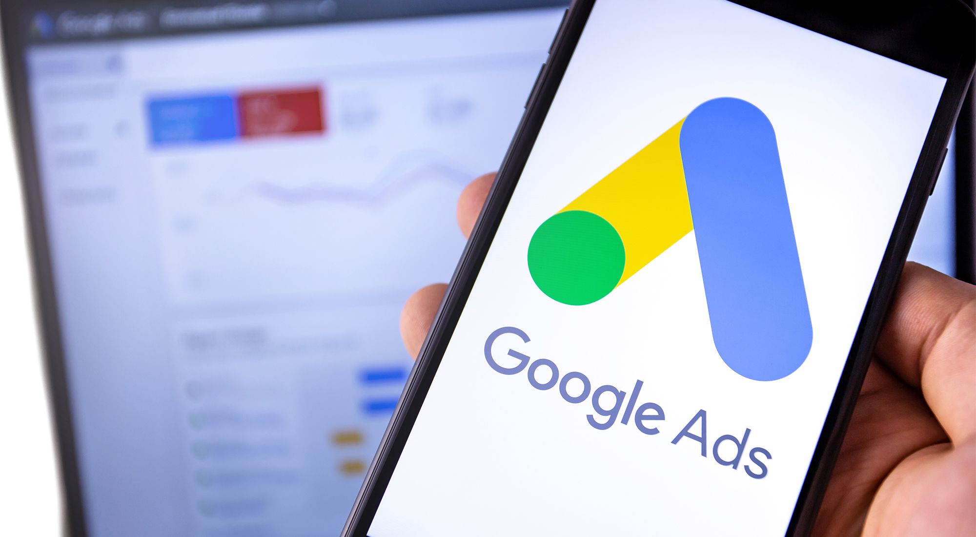 Google Ads logo displayed on a smartphone screen placed on a blurry metrics background. 