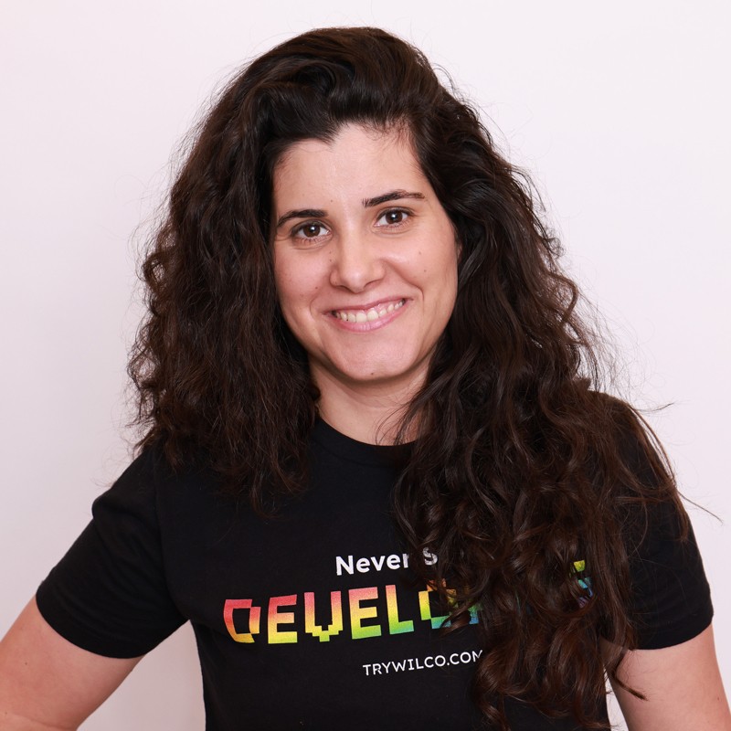 Mujer sonriente de pelo oscuro y rizado con una camiseta negra con estampado gráfico sobre un fondo pálido.