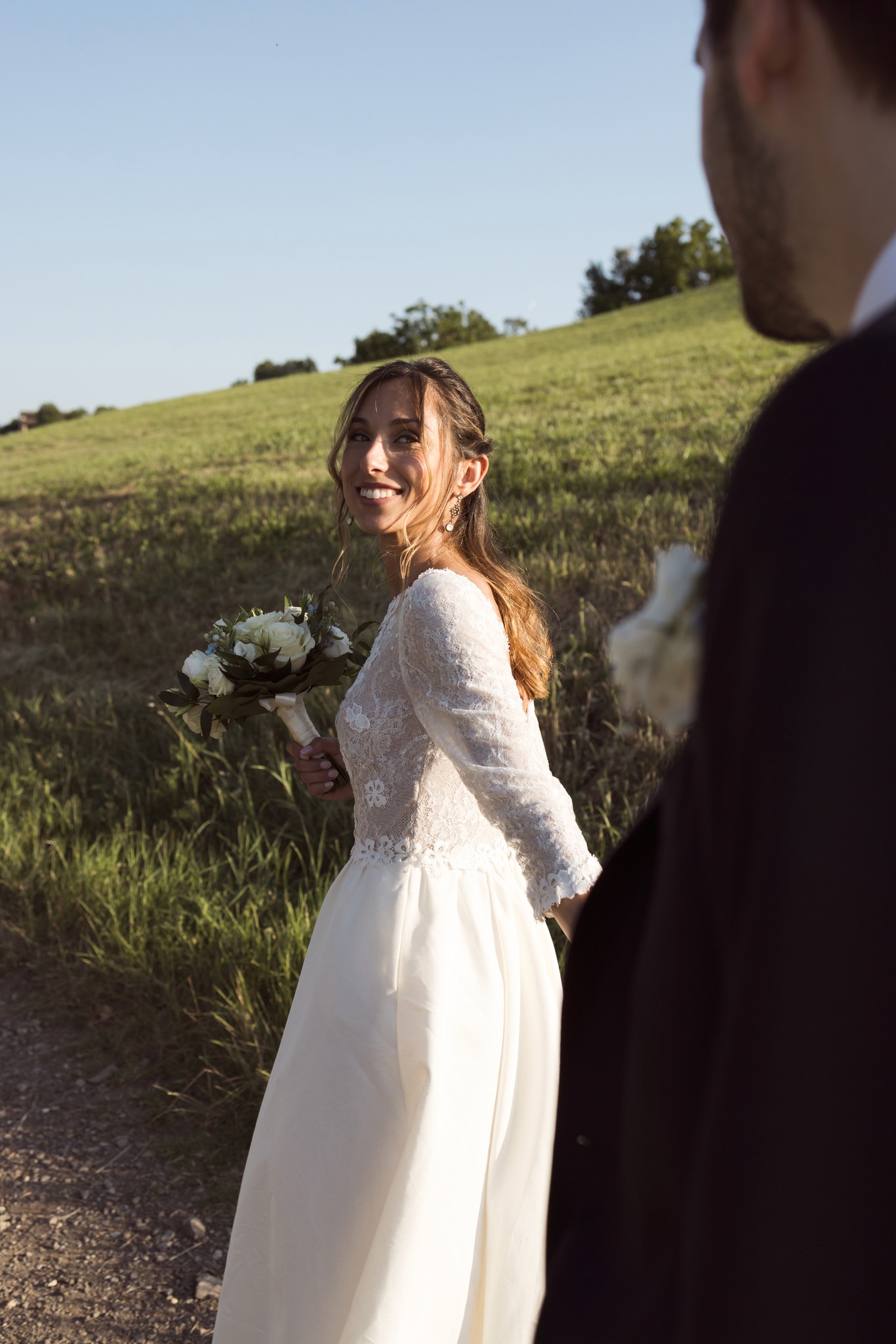 Sposa in abito bianco con bouquet sorride allo sposo nei campi di Villa Peroni Riva, reportage matrimoniale in Emilia-Romagna