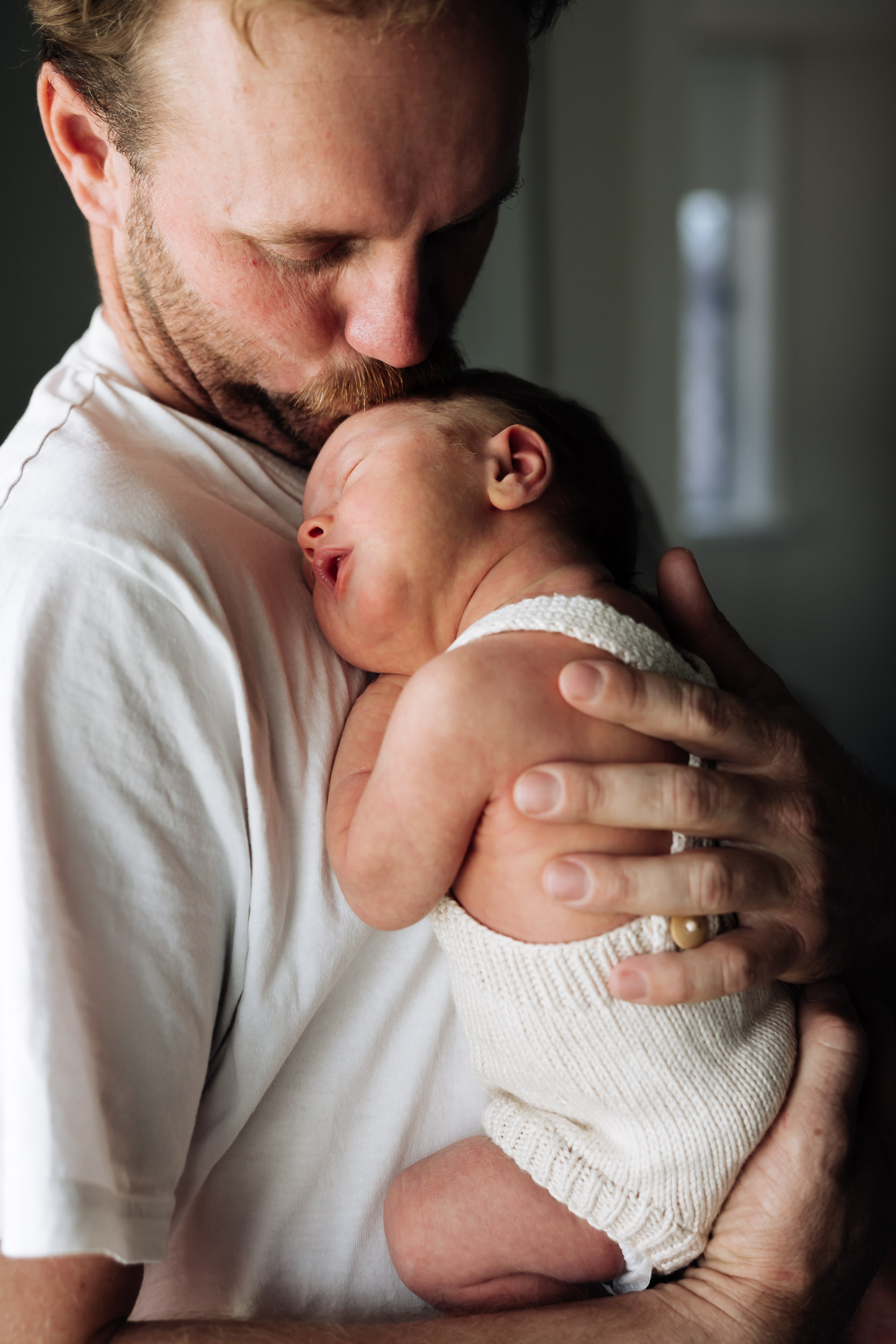 Father holding and kissing his newborn baby on the top of the head