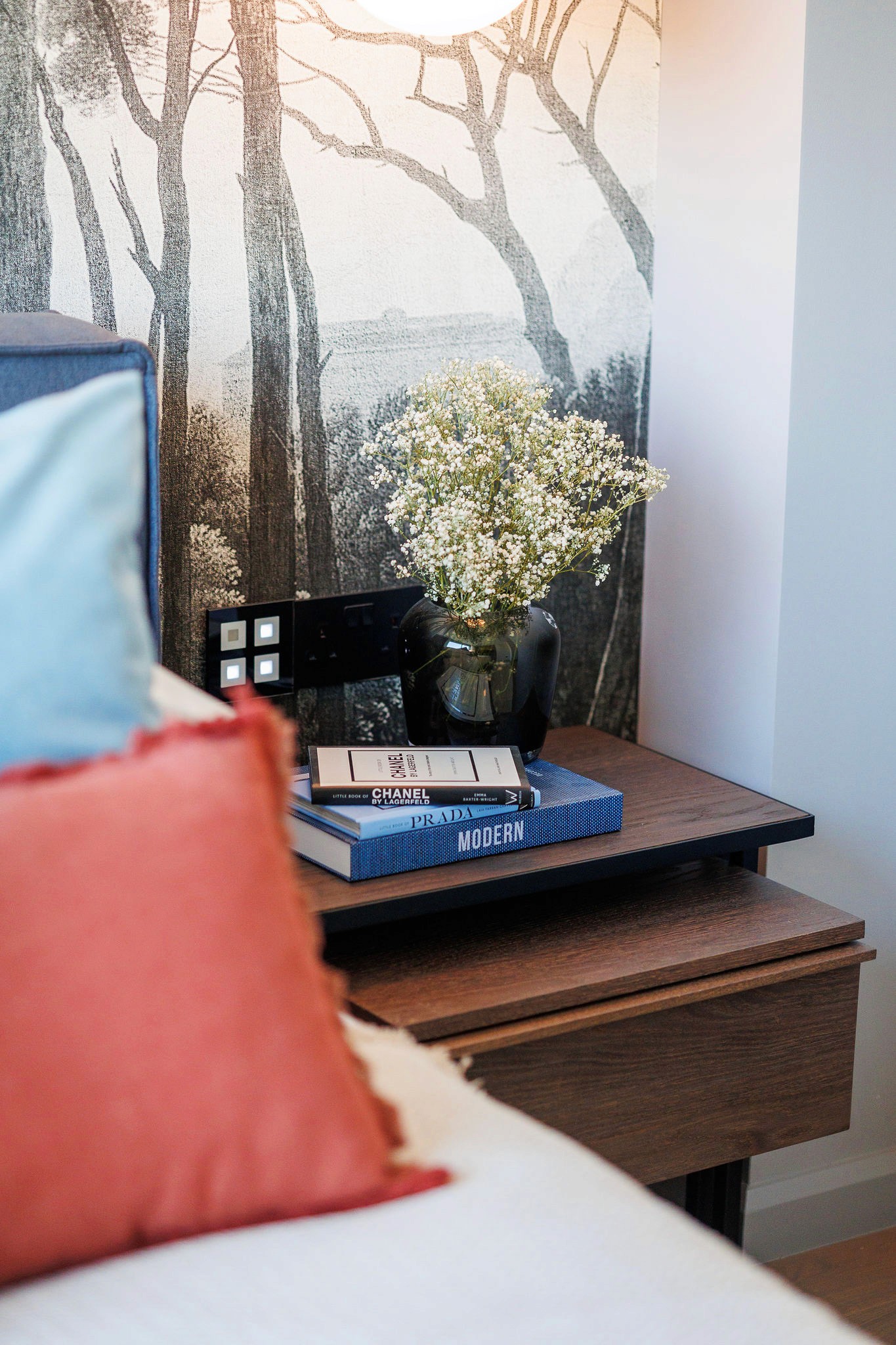 Villa Trio bedside styling with wooden nightstand, stacked books, and a vase of flowers