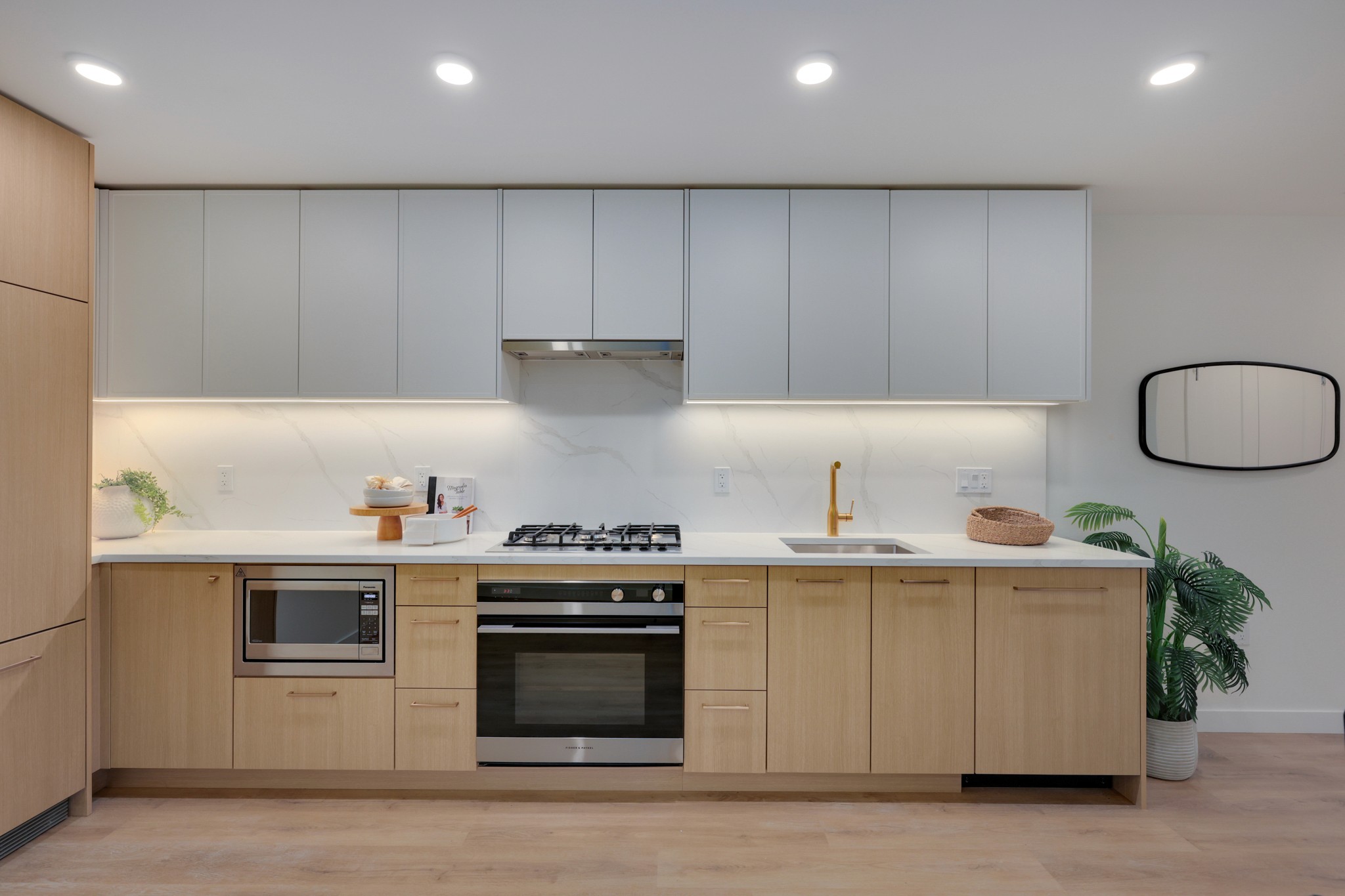 A modern kitchen with light wood cabinetry, sleek appliances, and bright overhead lighting.