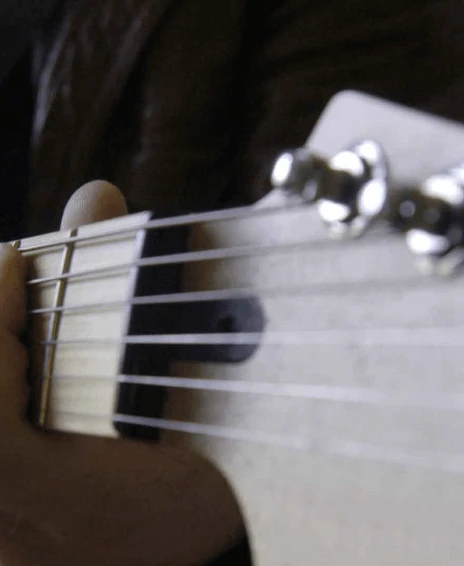 Close-up of a person's hand pressing down on guitar strings, focusing on the neck and tuning pegs of the instrument.
