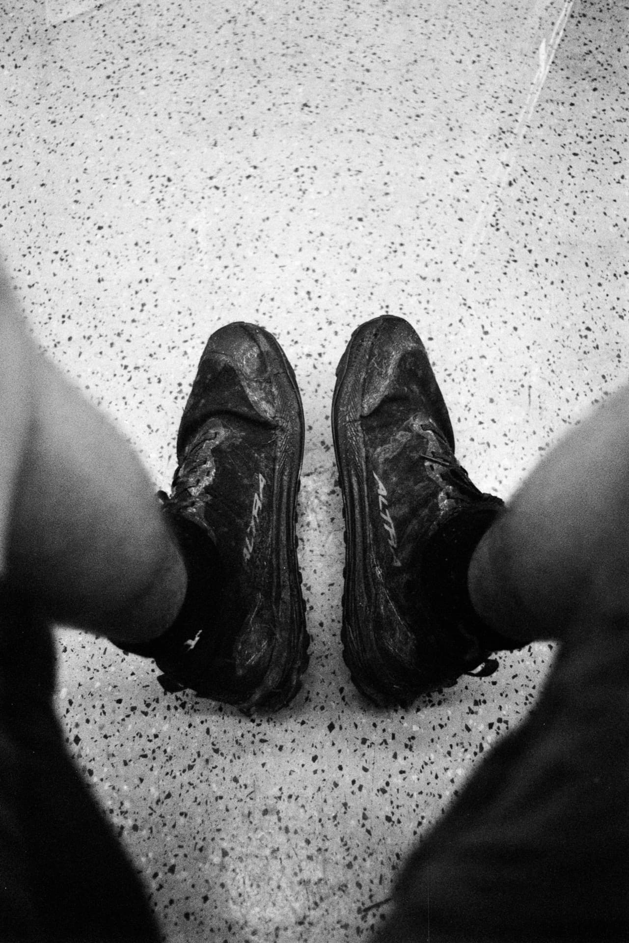 Mud-covered boots viewed from above on speckled train carriage floor after walking