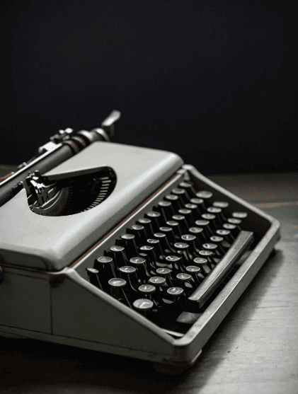 Close-up of a vintage blue typewriter with white keys, angled slightly to the left, against a warm beige background. The image evokes nostalgia.