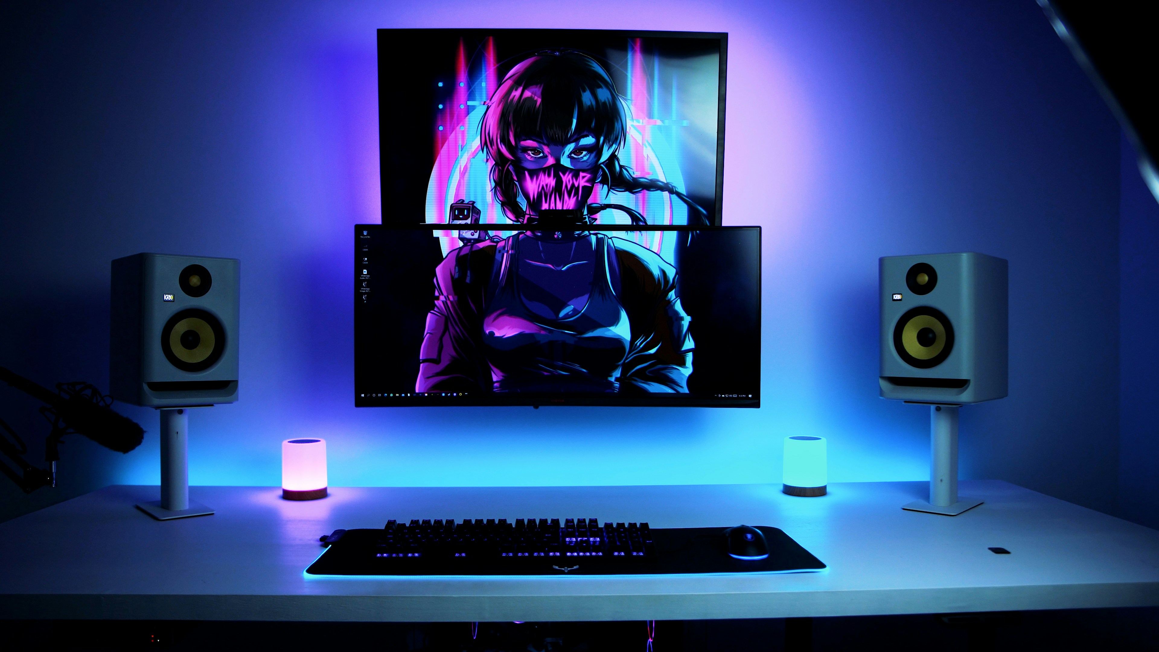 Modern gaming setup with a curved monitor displaying cyberpunk artwork, RGB lighting, keyboard, mouse, and two studio speakers on a white desk.