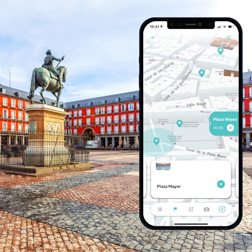 Duży ekran smartfona pokazujący mapę jest nałożony na widok na zewnętrzny plac z dużym pomnikiem konnym i czerwonymi budynkami.