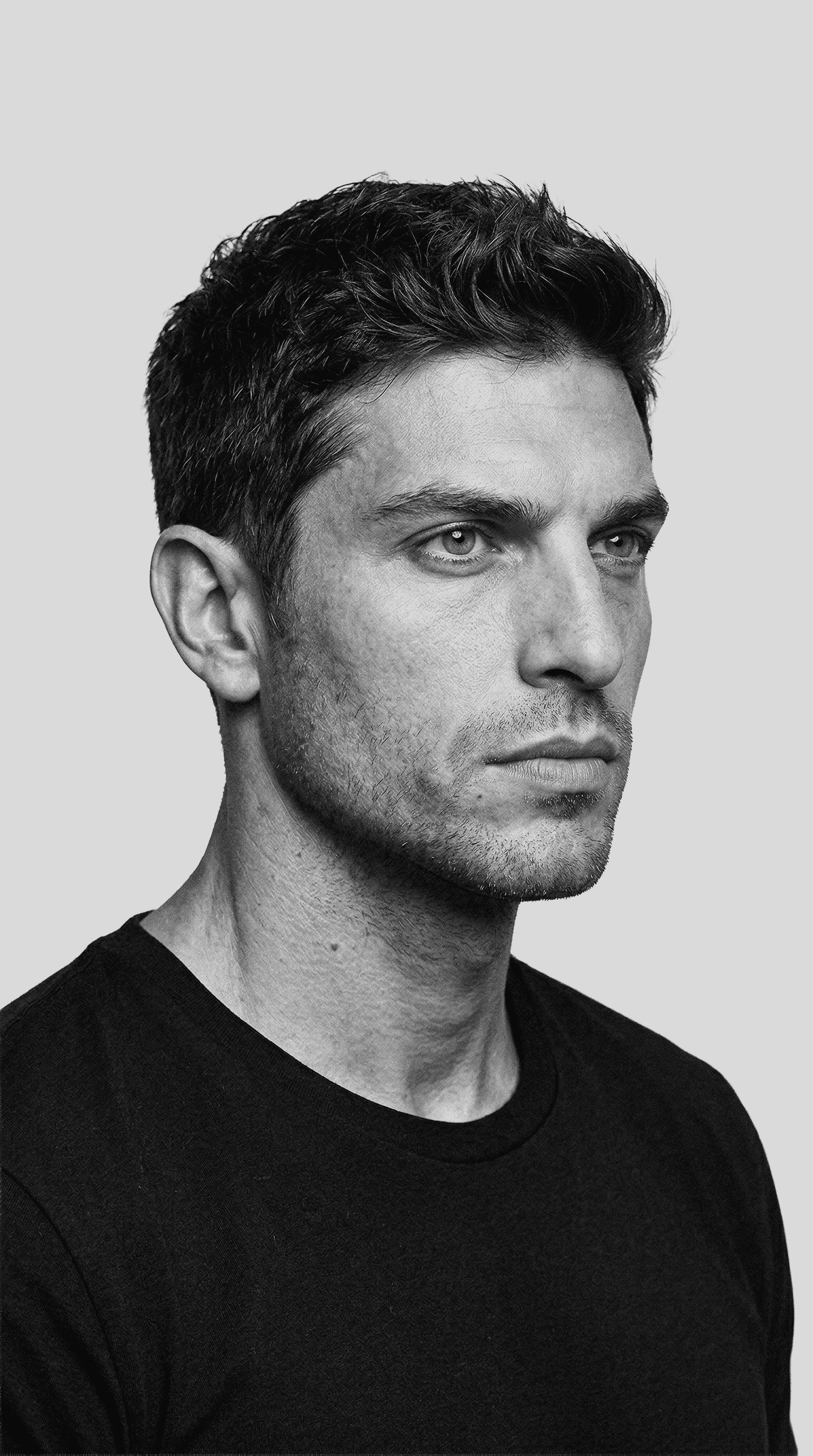 Portrait of a young man with short hair, wearing a dark t-shirt, against a plain background.