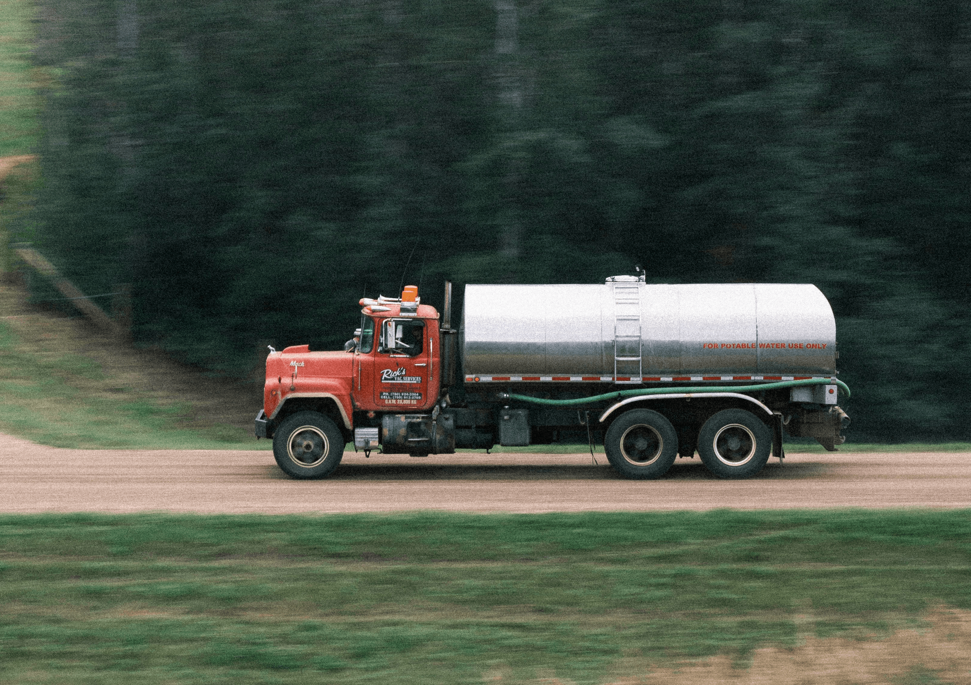 Red tanker truck driving down a dirt road.