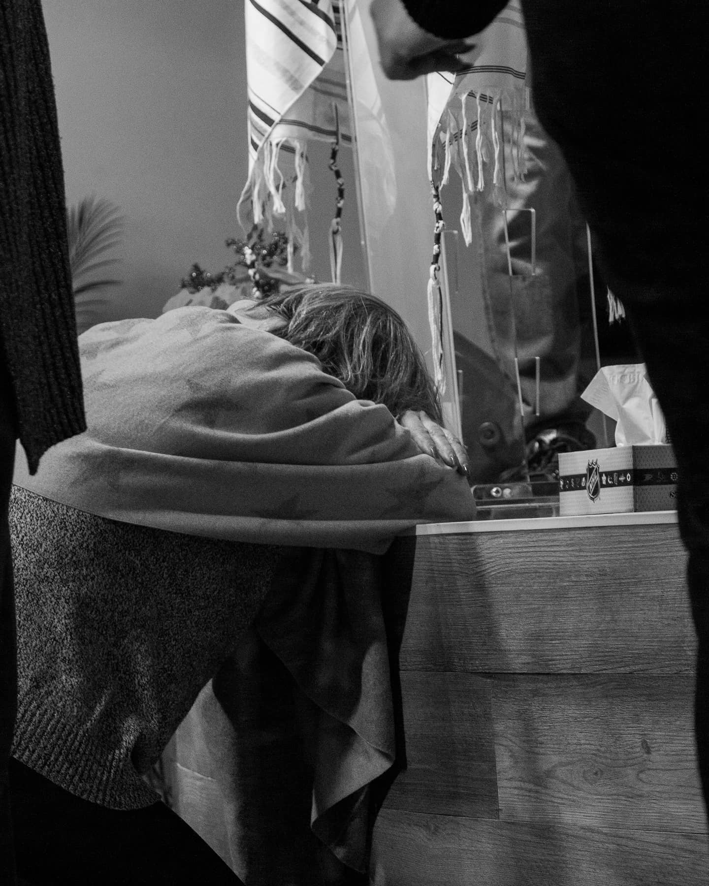 A smiling woman with her arms crossed, standing against a dark green background. She has long, dark hair.