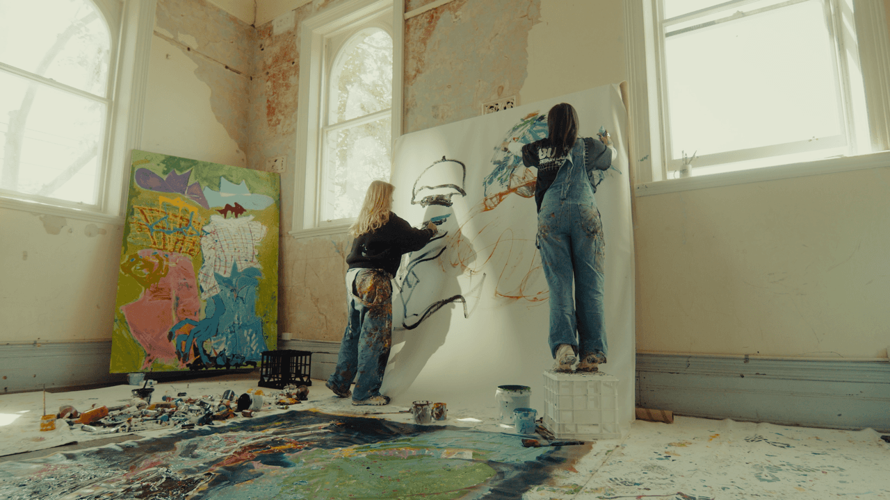Artists standing in front of a large canvas, working on abstract designs with splashes of color on the studio floor