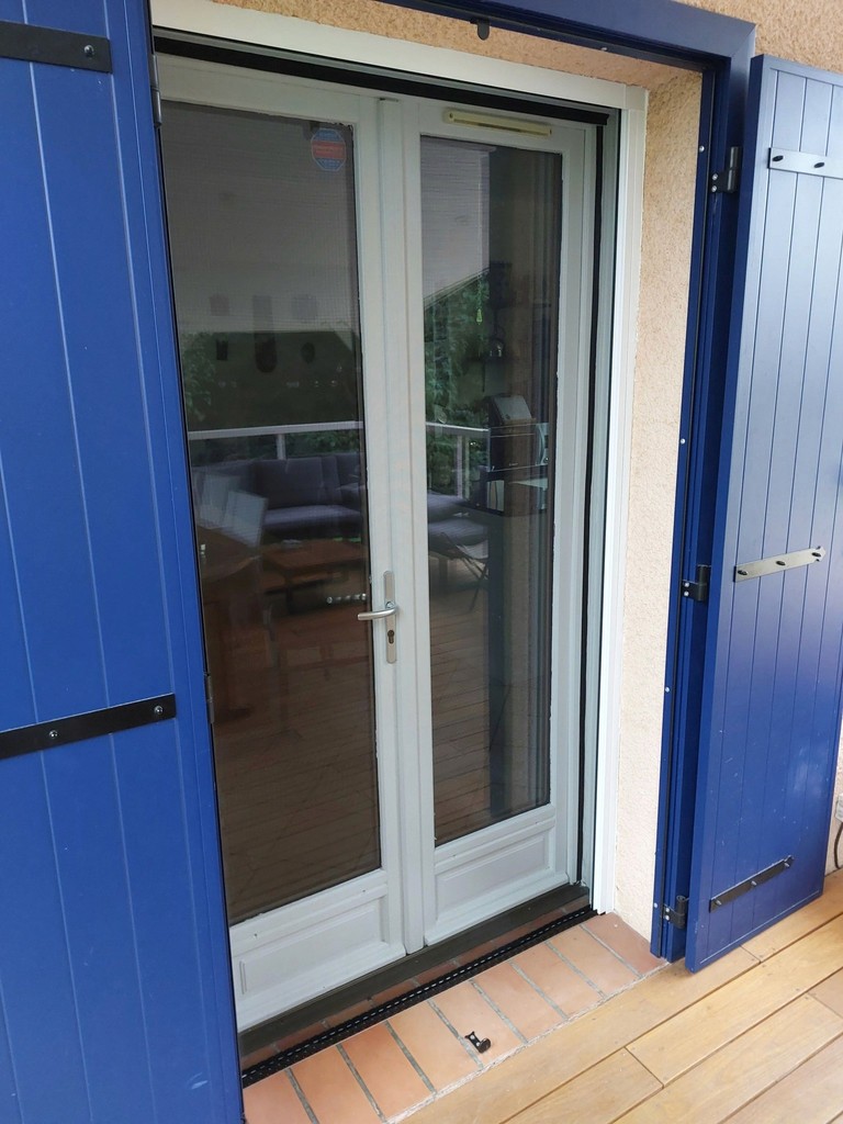 orte-fenêtre blanche à deux vantaux et volets bleus ouverts.