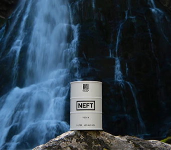 A NEFT Vodka white barrel in front of a rushing waterfall.