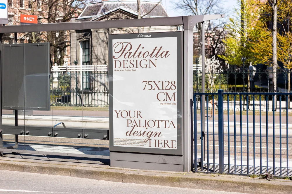 A bus stop advertisement panel displaying a vertical poster mockup with design specifications. The background includes metal railings, a tree-lined street, and historic buildings under a sunny sky.