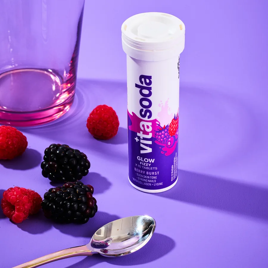 A Vita Soda Glow tube beside a pink glass with raspberries and blackberries