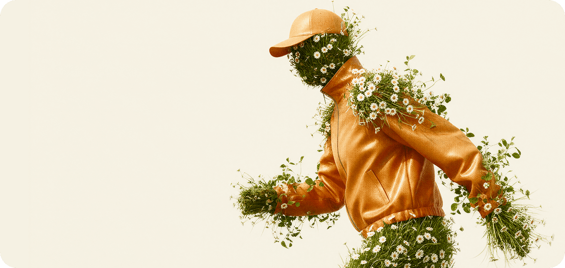A surrealist digital artwork of a floral figure in a dynamic walking or running pose, shown in profile. The figure wears a textured orange leather jacket and a matching orange cap. Their head, hands, and legs are entirely composed of thick green grass blooming with white daisies, with extra clusters of flowers and green vines sprouting from the shoulders and seams of the jacket against a plain cream background.