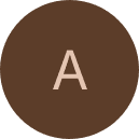 Portrait of a young woman with dark hair and green eyes, wearing a black top and gold necklace, set against a neutral background.