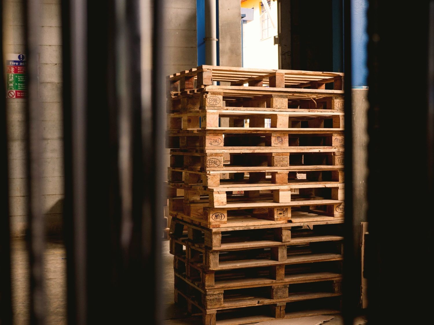 A stack of wooden pallets, marked with "EPAL," is positioned in an industrial setting. Dim lighting creates a rustic, warehouse atmosphere.