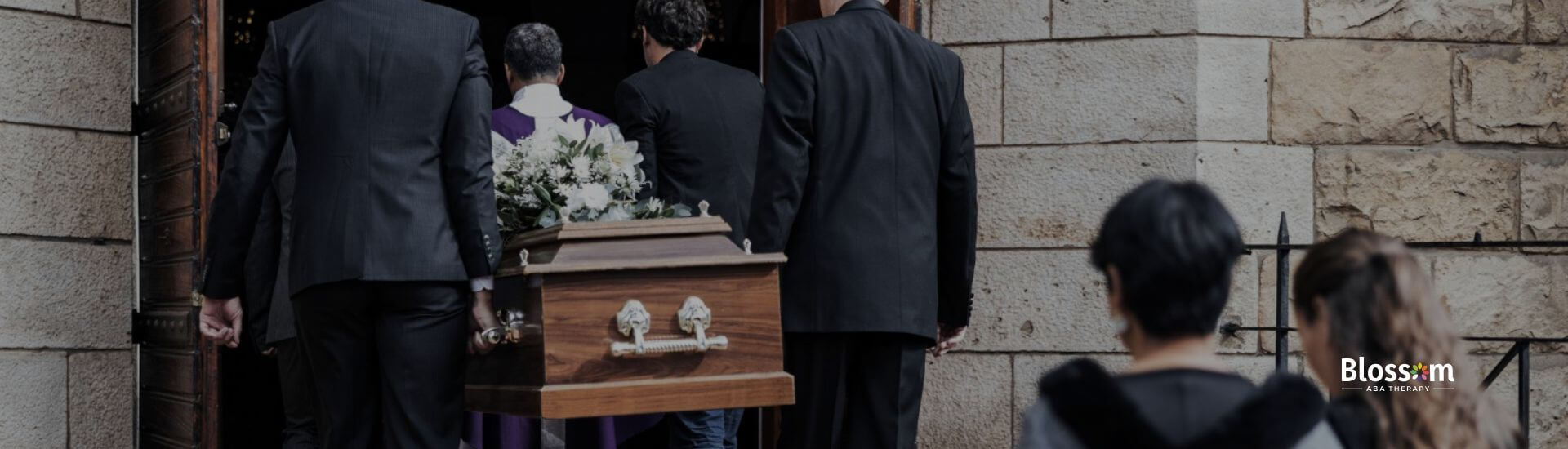 Pallbearers carrying a wooden casket into a church as mourners follow behind.