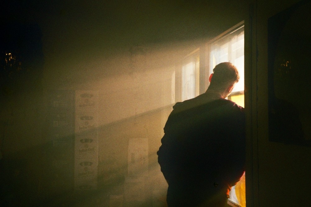 Back view silhouette of a young person looking out a window at sunrise in analog photography