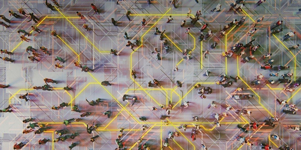 Top-down aerial view of a diverse crowd of people walking across a light grey surface overlaid with glowing yellow and grey digital circuit board patterns and data lines.