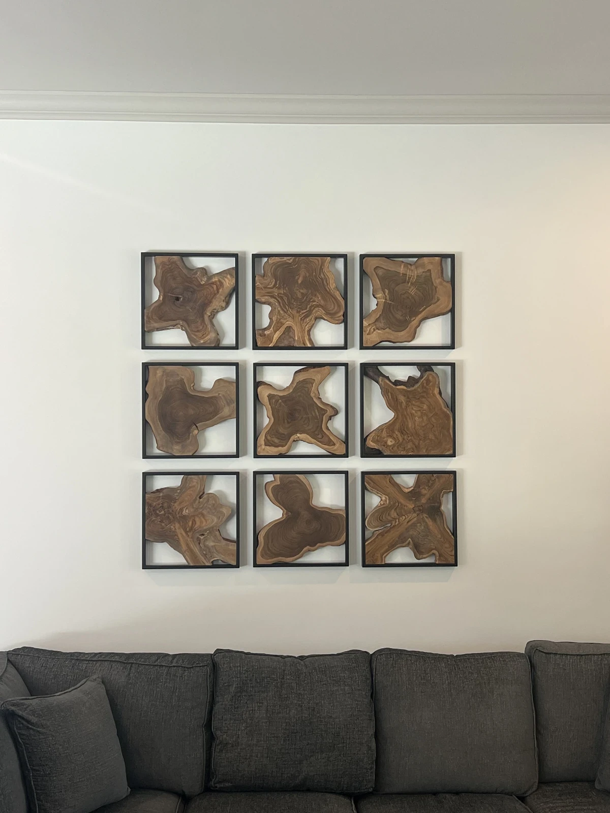Nine framed wood artworks installed in an evenly spaced three-by-three gallery above a sofa.
