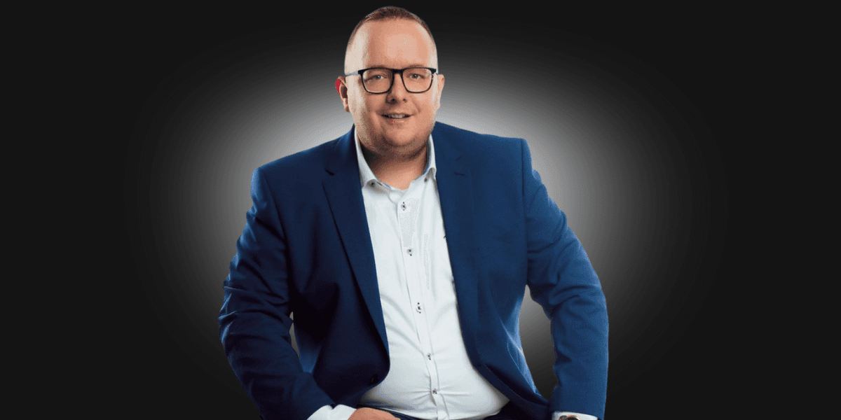 A professional man in a blue suit, smiling and sitting confidently, representing Toldi Marketing's focus on sustainable business growth.