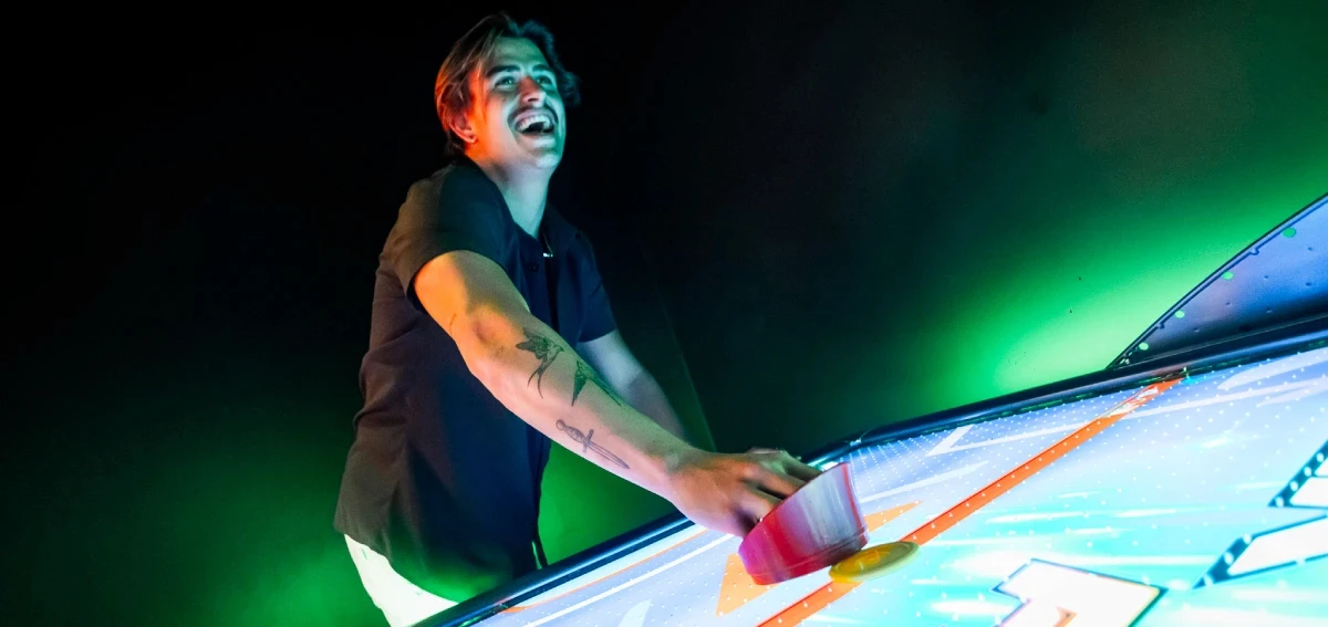 A man laughing mid game at a green lit air hockey table